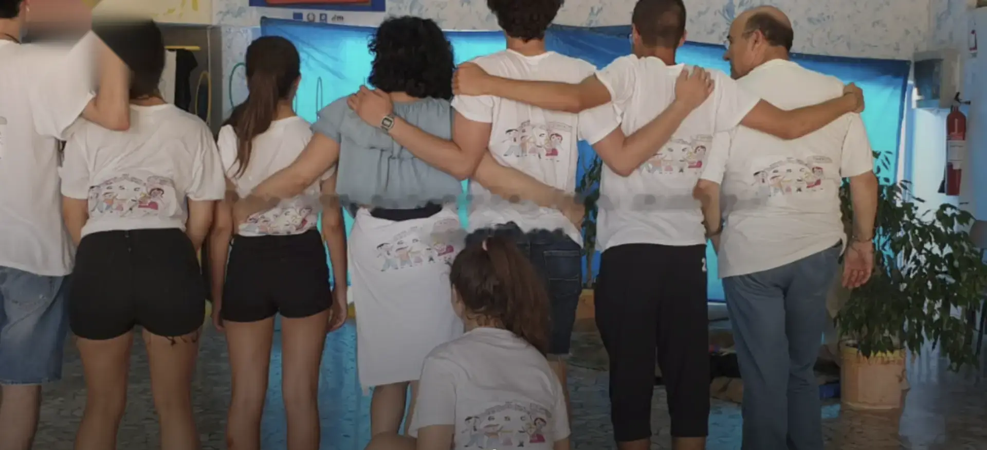 Volontarie, volontari e ragazzi dell’associazione abbracciati di spalle, con le magliette disegnate dai bambini